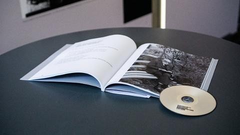 Der Ausstellungsband der Gedenkstätte liegt geöffnet auf einem grauen Tisch. Auf dem Buch liegt eine CD.